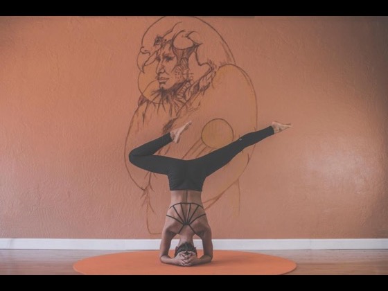 A yoga studio with warm terracotta walls, one person balancing in a supported headstand on a mat.